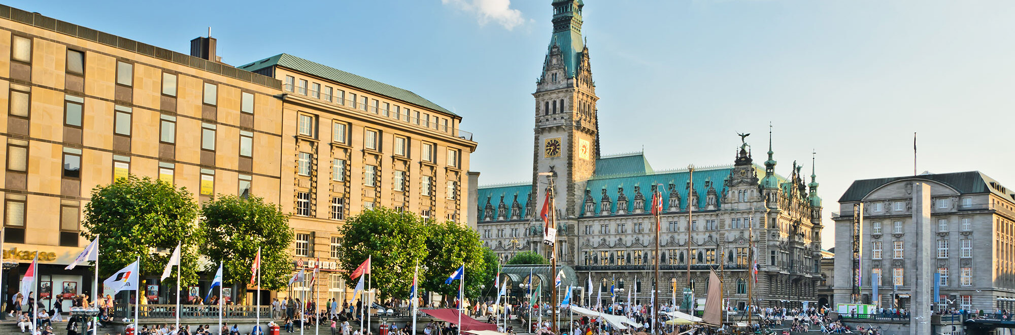 Ein belebter Platz am Wasser in Hamburg mit dem Hamburger Rathaus im Hintergrund.